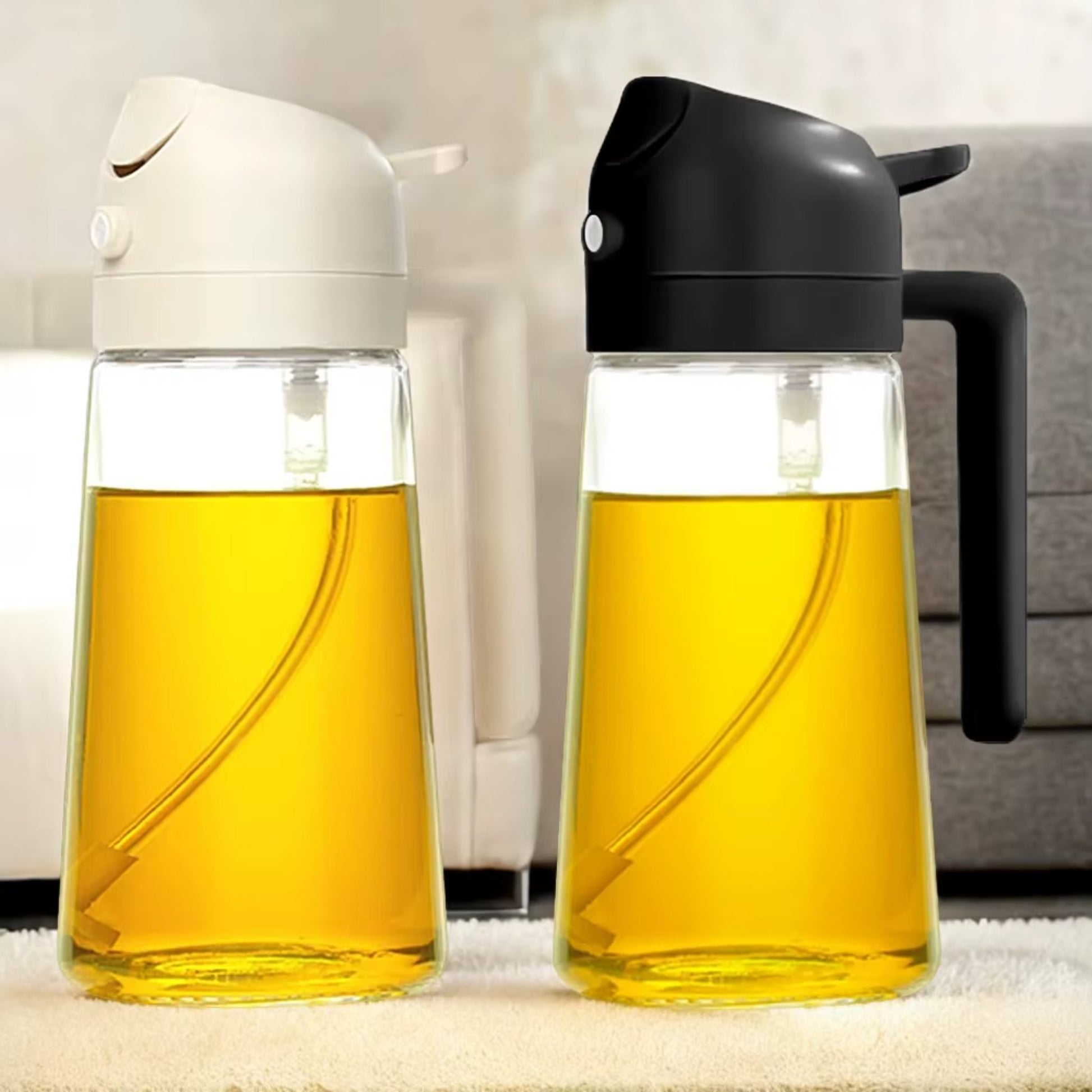 Two clear oil dispensers with black and white gravity-sensor lids placed on a countertop, filled with golden liquid.