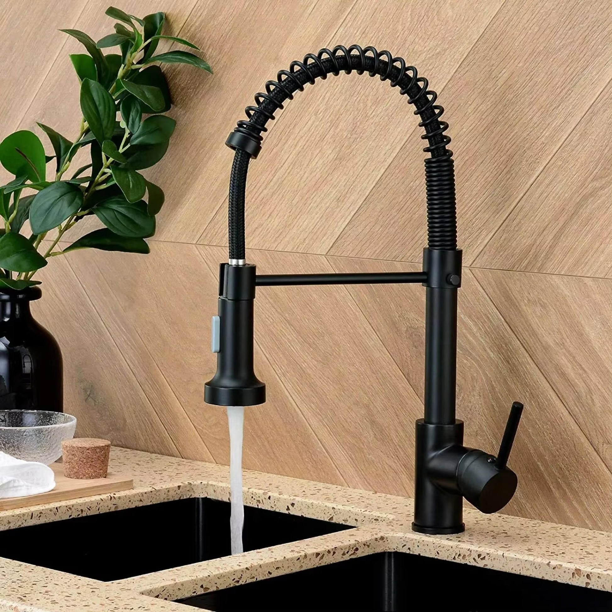 Modern matte black kitchen faucet with a coiled spring design, running water, set against a light wooden backsplash.