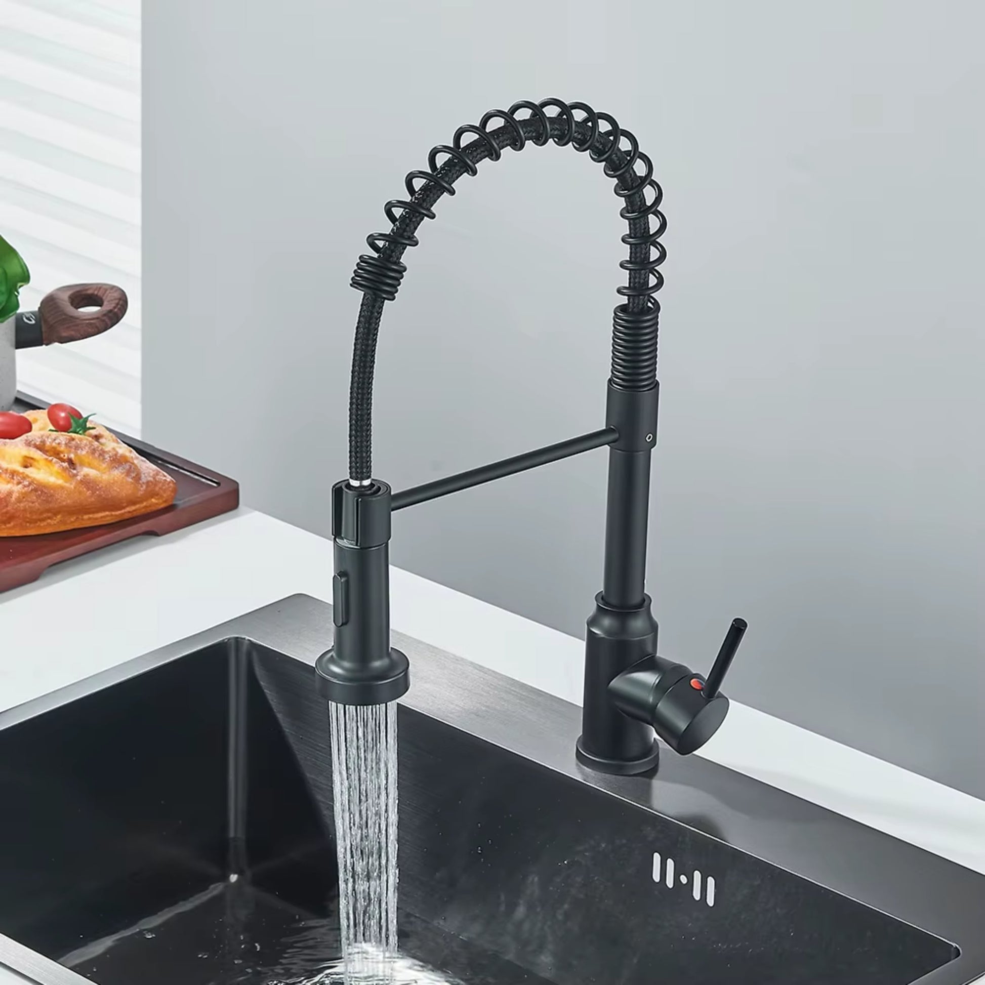 Matte black kitchen faucet with water flowing into a modern sink, accompanied by a cutting board and bread in the background.