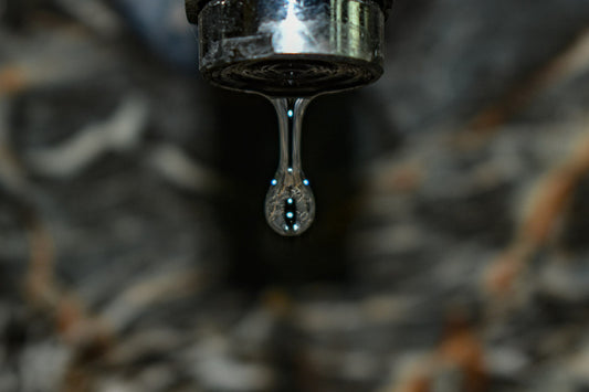 Close-up of a faucet head with a single water droplet falling from it.